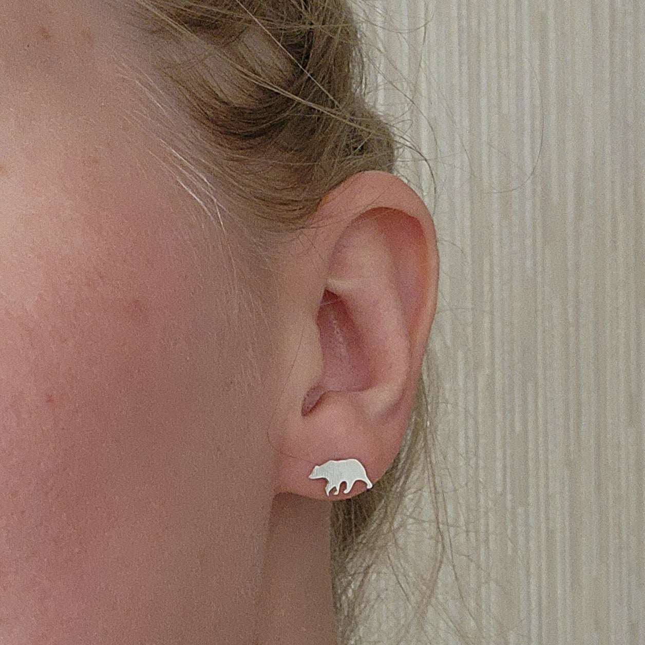 sterling silver bear stud earrings with silicone backs, in left ear with bear facing towards face